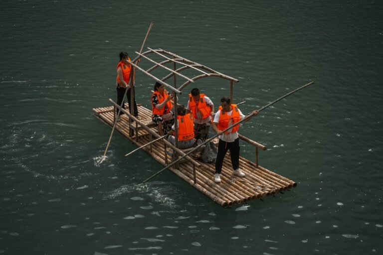 A team enjoys rafting on a bamboo raft wearing safety vests on calm waters.