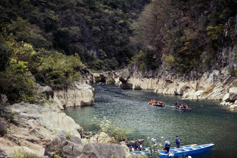 People kayaking through a scenic canyon river, surrounded by lush greenery and rocky landscape.